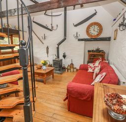 A living room with a red sofa wooden spiral staircase and a wood burning stove at Heather Cottage in Rosemarket
