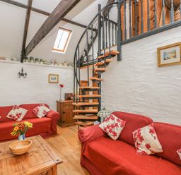 A living room with two red sofas and a wooden spiral staircase at Heather Cottage in Rosemarket