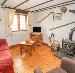 A living room with a red sofa a wood burning stove and wooden furniture at Cowslip Cottage in Rosemarket