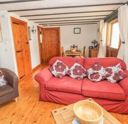 A living room with a red sofa and floral cushions a wooden dining table and chairs a brown armchair and wooden doors at Cowslip Cottage in Rosemarket