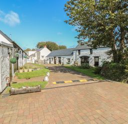 An outdoor paved driveway with white buildings on both sides and trees at Primose Cottage in Rosemarket
