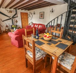 A dining and living area with a wooden table and chairs a red sofa and a black spiral staircase at Primose Cottage in Rosemarket