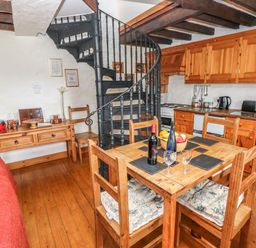 A kitchen and dining area with wooden furniture a spiral staircase and kitchen appliances at Primose Cottage Rosemarket