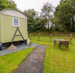 A green shepherds hut with a path leading to a table and chairs on grass at Shepherds Hut - The Crook in Rosemarket near Neyland