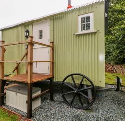 An exterior view of a green shepherds hut with wooden steps and black wheels at Shepherds Hut - The Crook in Rosemarket near Neyland