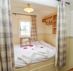 A small bedroom with a bed linens folded towels and a window at Shepherds Hut - The Crook in Rosemarket near Neyland