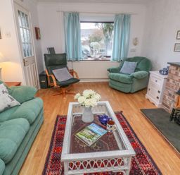 A living room with green armchairs a wooden coffee table with flowers and magazines a fireplace and a window with blue curtains at Phenests in Falmouth