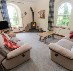 A living room with two sofas a wooden coffee table a wood burning stove and a television at Beggars Roost in Penhallow