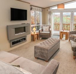 A living room with armchairs a sofa a wall-mounted tv and fireplace and a window showing an outdoor view at Avonal Lodge 24 in Dunning