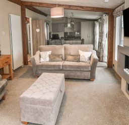 A living room with a sofa a chair an ottoman a wall-mounted TV and a wooden side table at Avonal Lodge 24 in Dunning