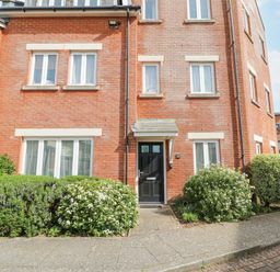 A brick apartment building with a black front door and white framed windows surrounded by bushes at Admirals Quarter Apartment 4 in Weymouth