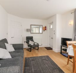 A living room with a grey sofa a black armchair a wooden dining table with chairs and a television at Admirals Quarter Apartment 4 in Weymouth