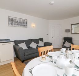 A dining table set with plates and cups next to a kitchen area and a living room with a sofa and armchair at Admiral's Quarter Apartment 4 Weymouth