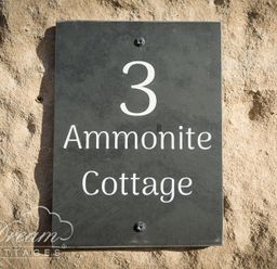 A black metal house number sign with the number 3 and text Ammonite Cottage on a rough stone wall at Ammonite Cottage Fortuneswell Portland