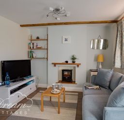 A living room with a television on a white stand a gray sofa a small wooden coffee table and a fireplace at Ammonite Cottage Fortuneswell Portland