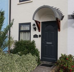 Front door of a house with a black door and curved awning surrounded by plants at Anvil House Brewers Quay Harbour