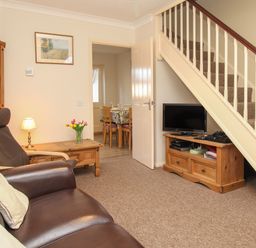 A living room with a brown leather sofa and armchair wooden furniture and a television under the stairs at Anvil House in Brewers Quay Harbour