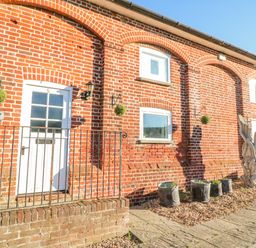 The exterior of a brick building with a white door and windows with hanging plants and potted plants at Barley Mews Brewers Quay Harbour