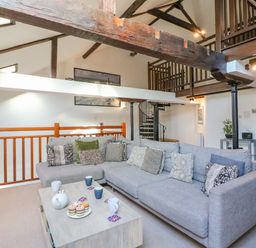 A living room with a large grey sectional sofa and a wooden coffee table with tea set and cupcakes at Barley Mews Brewers Quay Harbour
