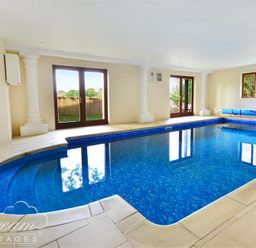 An indoor swimming pool with steps leading into the water and windows showing an outdoor view at Baytree Lodge in Osmington