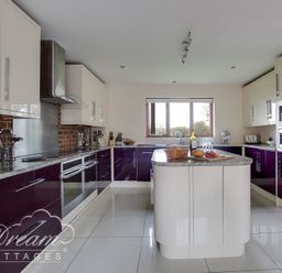 A kitchen with white and purple cabinets a central island and a window at Baytree Lodge in Osmington