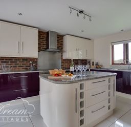 A kitchen with white and purple cabinets a central island with wine glasses and a basket of bread at Baytree Lodge in Osmington