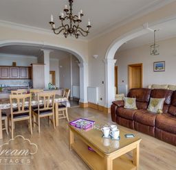A living room with a brown leather sofa a wooden coffee table and a dining area with chairs and a table at Beach View Apartment 2 in Greenhill