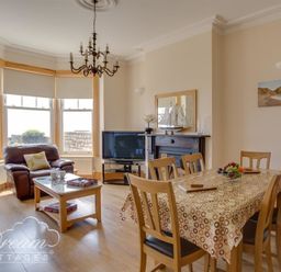 A living room with a dining table and chairs a sofa a coffee table a television and a fireplace at Beach View Apartment 2 in Greenhill