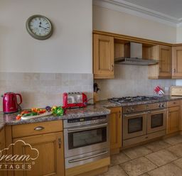 A kitchen with wooden cabinets a red kettle and toaster a wall clock and stainless steel ovens at Beach View Apartment 2 in Greenhill