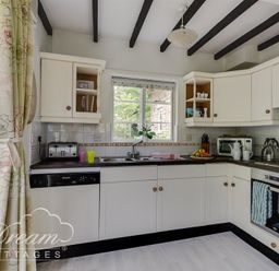 A kitchen with white cabinets black countertops a window above the sink and kitchen appliances at Little Berwick Cottage Burton Bradstock