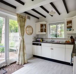 A kitchen with white cabinets a window over the sink and glass doors leading outside at Little Berwick Cottage in Burton Bradstock