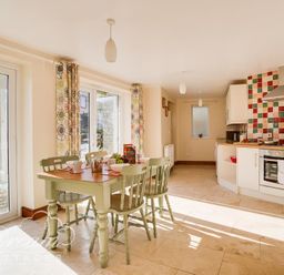 A kitchen with a dining table and chairs next to large windows and tiled backsplash at Blueberry Cottage in Sutton Poyntz