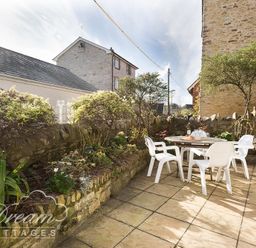 An outdoor patio with a round table and four white chairs surrounded by stone walls and plants at Blueberry Cottage in Sutton Poyntz