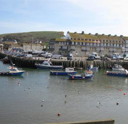 A harbor with boats on the water and buildings along the shore with a hill in the background at The Boardwalk in West Bay
