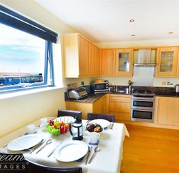 A kitchen with wooden cabinets a dining table set with plates cutlery and a fruit bowl at The Boardwalk in West Bay