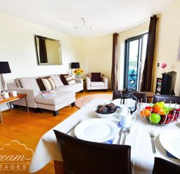 A dining table set with plates cups and fruit bowls next to a living area with sofas lamps and a mirror at The Boardwalk in West Bay