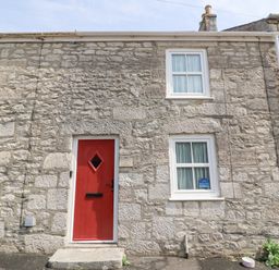 A stone house exterior with a red door and white framed windows at Bowmans Cottage in Wakeham Portland