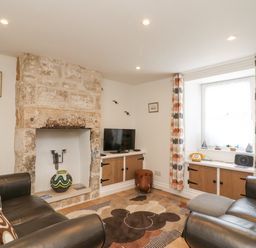A living room with leather sofas stone fireplace curtains and a TV at Bowmans Cottage in Wakeham Portland