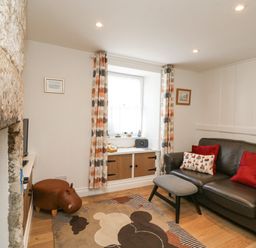 A sitting room with a black leather sofa red cushions a patterned rug and a window with patterned curtains at Bowman's Cottage in Wakeham Portland