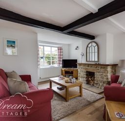 A living room with red sofas a wooden coffee table and a stone fireplace at Bramble Cottage in Burton Bradstock