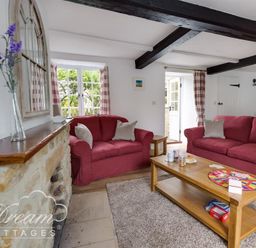A living room with red sofas wooden coffee table and stone fireplace at Bramble Cottage in Burton Bradstock
