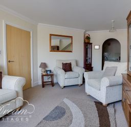 A living room with three armchairs a wooden cabinet and a small side table at Bridge Apartment in Weymouth