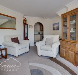 A living room with two armchairs a wooden cabinet and a side table with a lamp at Bridge Apartment in Weymouth