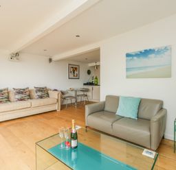 A living room with two sofas a glass coffee table with champagne and glasses a small dining table and chairs at Burton Bay in Burton Bradstock