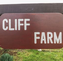 A wooden sign with white letters reading Cliff Farm mounted on a wooden fence with grass in the background at Cliff Farm No 2 Cottage in Burton Bradstock