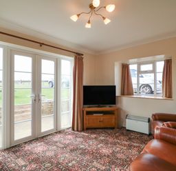 A living room with leather chairs a television on a wooden stand patterned carpet and French doors at Cliff Farm No 2 Cottage Burton Bradstock