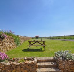 A picnic table with flowers and wine on a lawn with stone walls and flower beds at Cliff Farm No 2 Cottage Burton Bradstock
