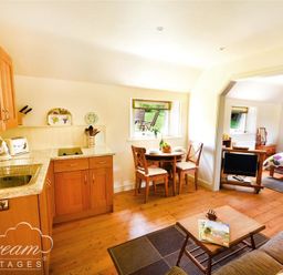 A small kitchen with wooden cabinets and a sink an adjoining dining area with a round table and two chairs then a bedroom with a bed a small TV and wooden furniture at Coombe Orchard in Swanage