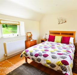 A bedroom with a double bed colorful bedspread and wooden furniture at Coombe Orchard in Swanage