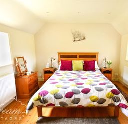 A bedroom with a double bed with patterned duvet and cushions beside wooden bedside tables at Coombe Orchard in Swanage